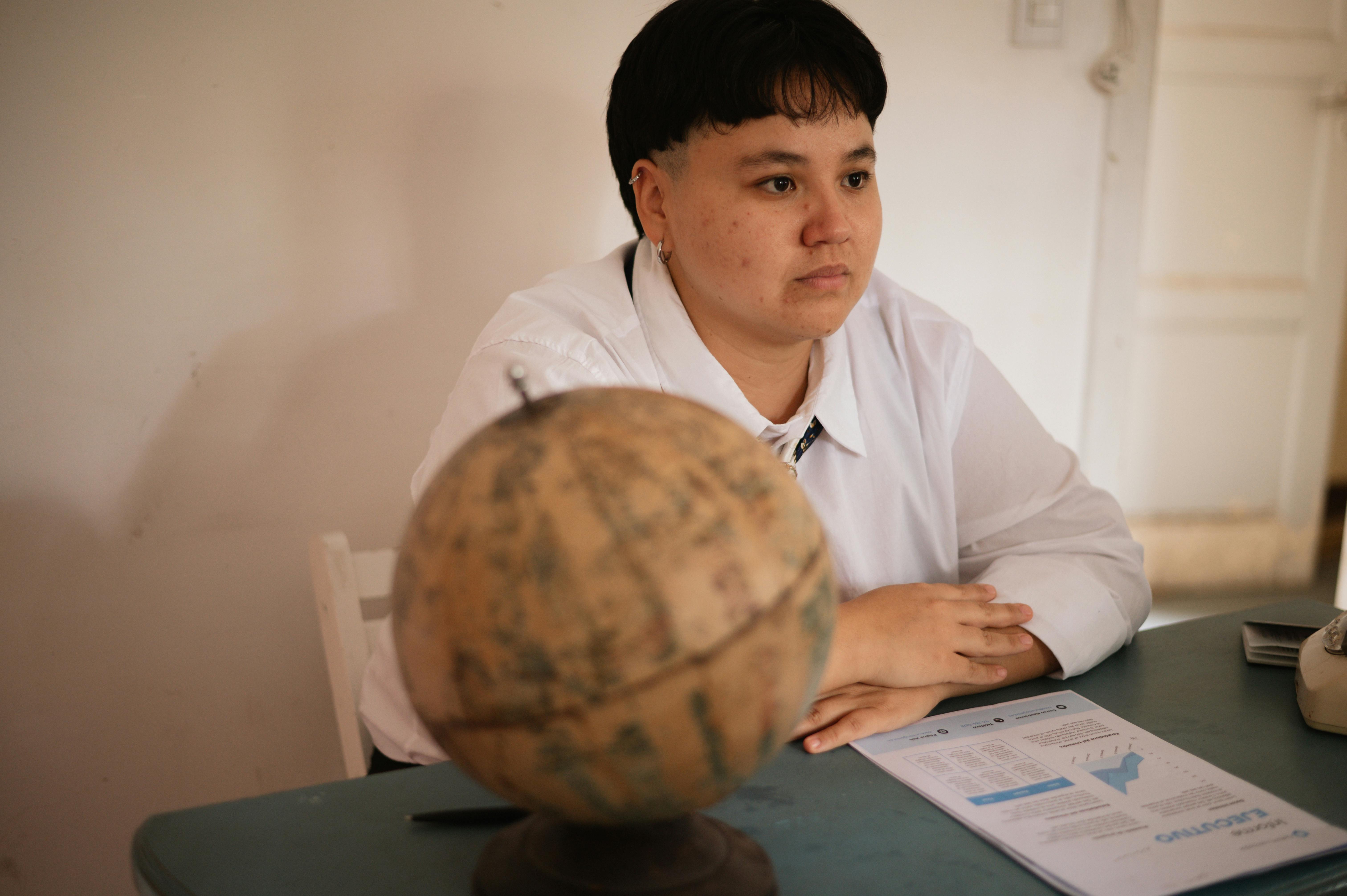 [A pharmacist holding a world map and travel vaccination information leaflet in a modern pharmacy consultation room]